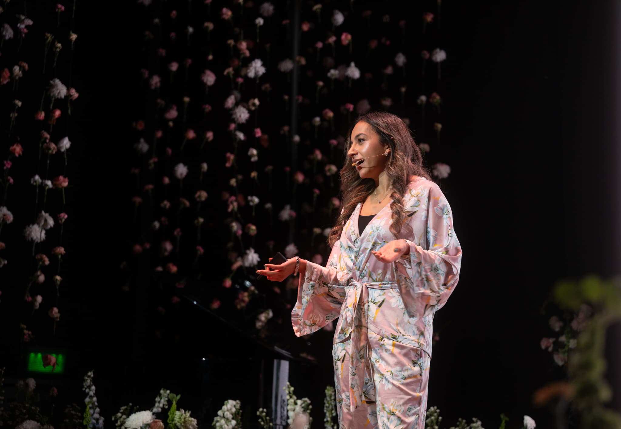 Speaking on stage before a curtain of suspended flowers