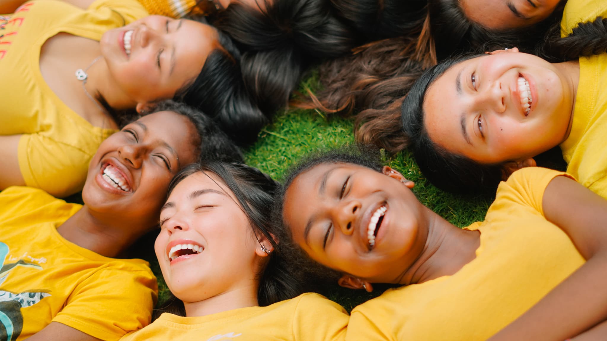 A circle of friends lying in the grass, laughing