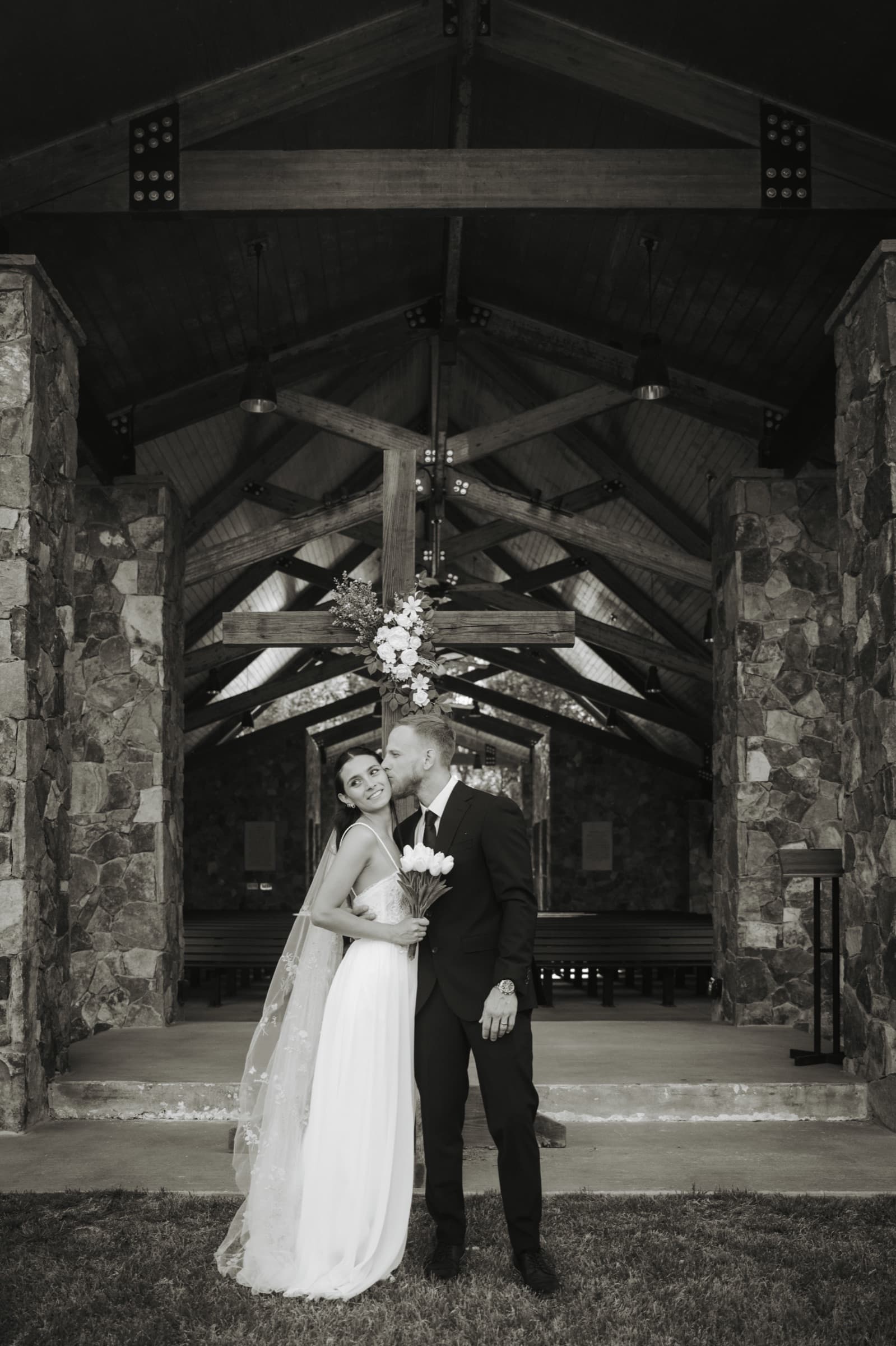 Groom kissing the bride's temple beneath the chapel cross