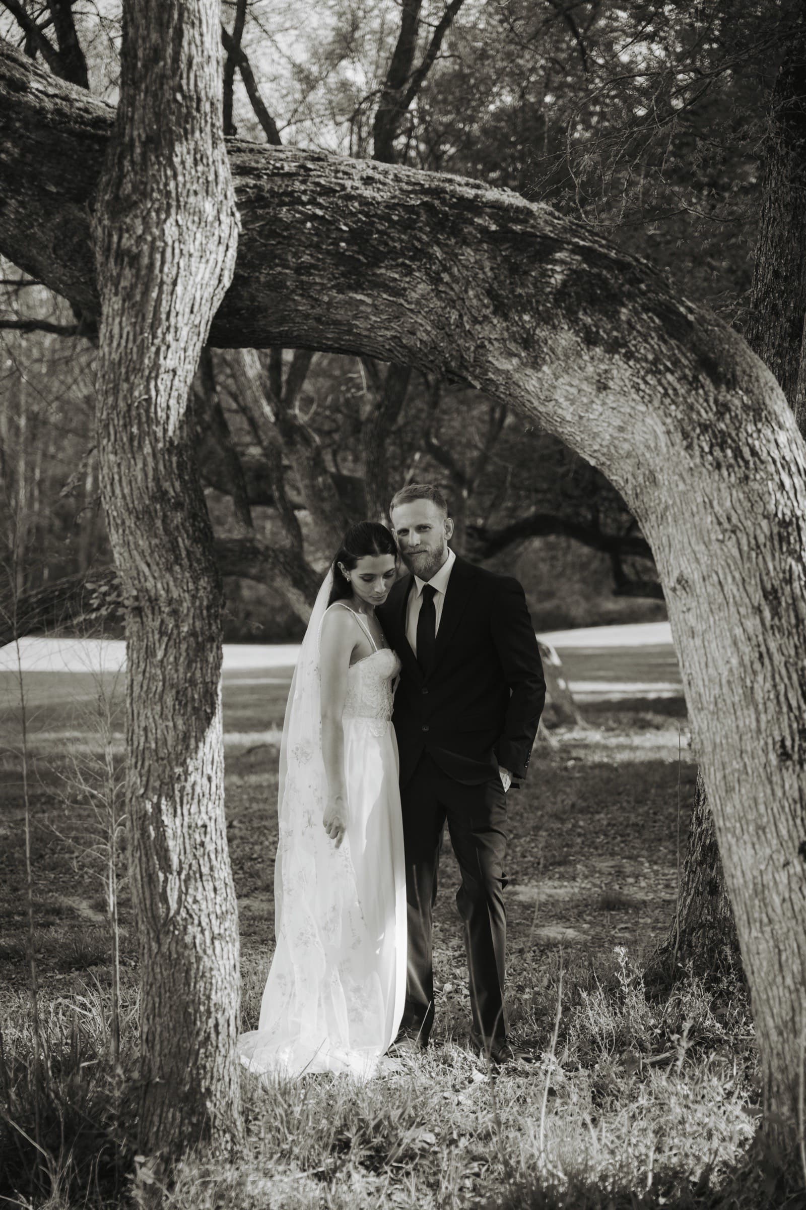 The bride rests against the groom beneath the trees