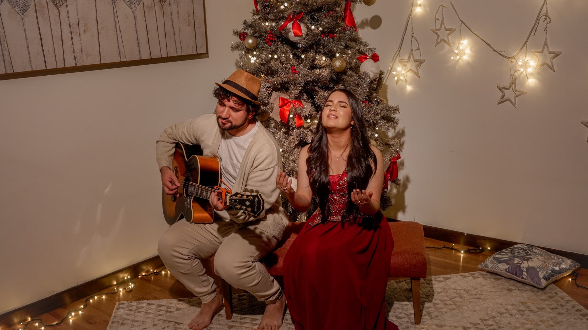 A guitarist and a singer performing beside a lit Christmas tree