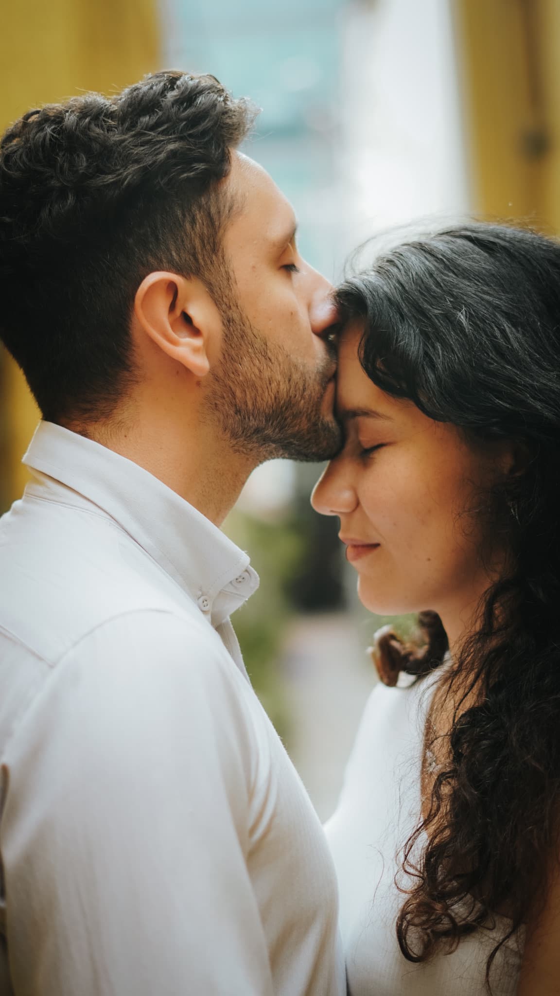 A kiss to her forehead in a sunlit alley, both in white