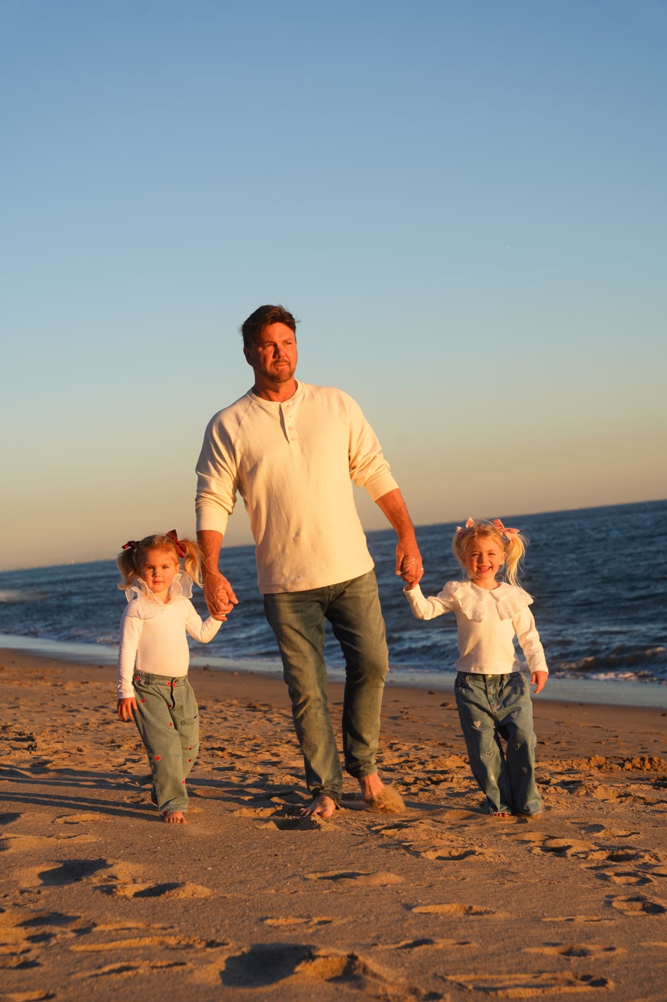 A father walking hand in hand with his two young daughters along the sand