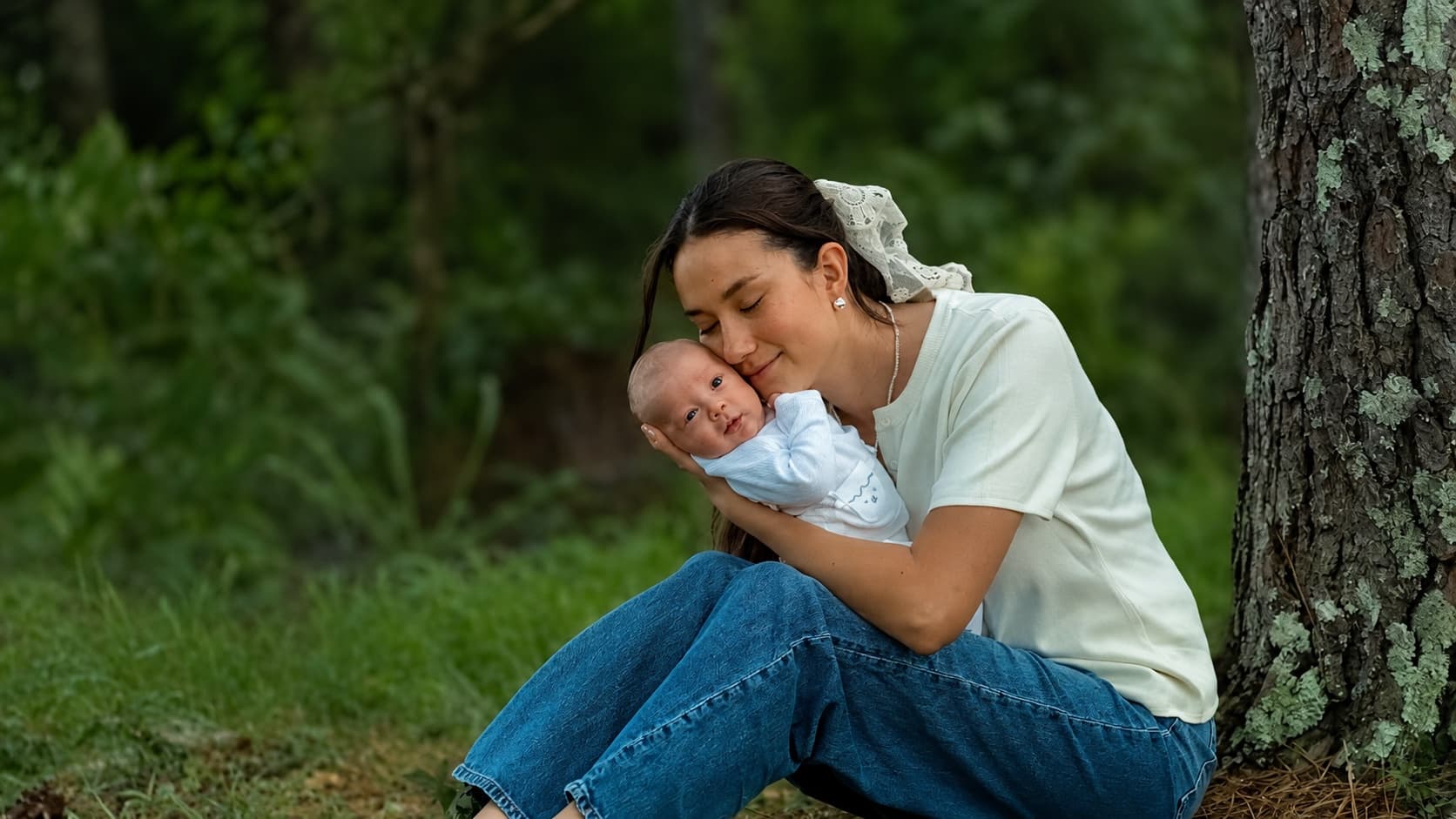 A mother holds her newborn close beneath a tree